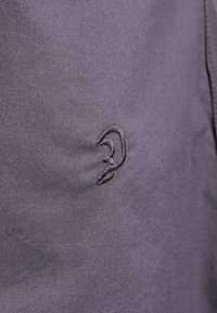 Gros plan sur un tissu foncé avec un symbole d’oreille cousu brodé avec un fil assorti sur la surface.