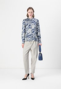 Blue patterned blouse with light gray tailored trousers. Black high heels and a small blue handbag complete the outfit. Simple design and textures.