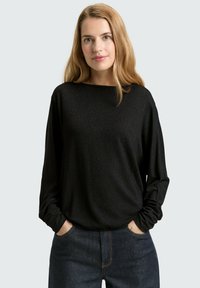 Zwarte long-sleeve top met een relaxte pasvorm, voorzien van een bootnek en zachte, gestructureerde stof. Gemaakt in combinatie met donkere spijkerbroeken.