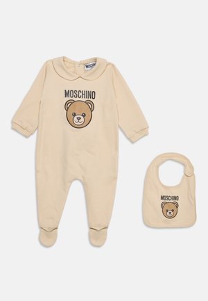 Ensemble beige body bébé et bavoir assorti avec col Claudine, logo Moschino et illustration visage d’ours en peluche à l’avant.
