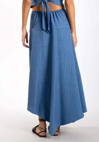 Larga falda azul hecha de una tela suave con un ligero brillo, con una cinturilla ancha y un dobladillo asimétrico con caída en la parte trasera.