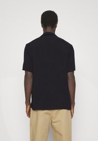 Camicia nera a maniche corte con colletto e vestibilità comoda, caratterizzata da tessuto liscio e taglio dritto all'orlo, abbinata a pantaloni beige.