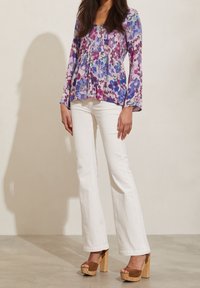 Blommig blus med långa ärmar, med lila och blå mönster, ihop med vita utsvängda byxor och bruna platåskor.