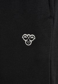 Schwarzer strukturierter Stoff mit einem kleinen weißen, bienenförmigen, gestickten Logo, das in der Mitte der Oberfläche angebracht ist.