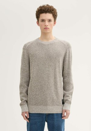 Hellbrauner Strickpullover mit Rundhalsausschnitt und gerippten Bündchen, der ein strukturiertes Muster und ein schwarzes Markenetikett am Saum aufweist.