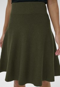 Gonna verde oliva, lunghezza ginocchio, realizzata in tessuto testurizzato con vita aderente e fondo svasato, caratterizzata da un taglio liscio e pulito.