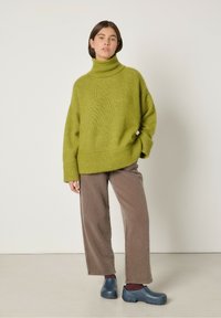 Roheline ülisuur salliga kootud sviiter, millele on sobitatud pruunid laiad küljelõigatud püksid ja sinised puuhobuserakmed. Lihtne tekstuur ja mugav lõige.