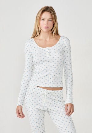 Completo pigiama coordinato a maniche lunghe in tessuto di cotone bianco con motivo floreale blu. Caratterizzato da un collo a barca e una vita regolabile con cordoncino.