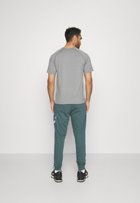 Grå kortermet skjorte kombinert med mørkegrønne joggebukser. Buksene har sidelommer og et subtilt mønster langs sidene.