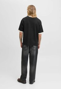 Camiseta negra con puños en crema contrastantes, combinada con unos jeans gris de corte holgado. Diseño sencillo, tejido suave y silueta relajada.