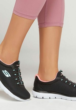 Nogi ubrane w różowe krótkie legginsy i czarne sportowe buty Skechers z białą podeszwą i jasnoniebieskimi akcentami na sznurowadłach.