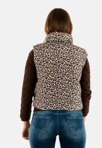 Camisa marrón de manga larga de punto acolchado combinada con un chaleco de estampado de leopardo en beige y negro, que presenta un cuello alto y una silueta ajustada.
