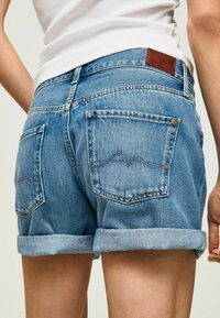 Džínové šortky s lehce modrým praním, ohrnutými lemy, zadními kapsami s kontrastním prošíváním a hnědou koženou značkou na pásu.