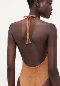 Brown suede one-piece swimsuit with a low back and tie closure at the neck. Smooth texture and minimalistic design.