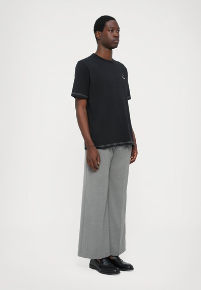 Tricou negru din bumbac cu mâneci scurte și guler rotund, asociat cu pantaloni largi gri deschis și mocasini negri.