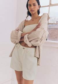 Pantaloncini verde chiaro abbinati a una camicia oversize a righe beige e bianche. La camicia ha le maniche arrotolate e una vestibilità casual.