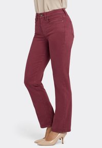 Bordeaux rode jeans met rechte pijpen en een gladde textuur, voorzien van een knoopsluiting aan de voorkant en zijzakken, gecombineerd met nude hoge hakken.