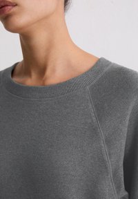 Szara bluza z okrągłym dekoltem, prążkowanym kołnierzem i teksturowaną tkaniną. Projekt obejmuje rękawy raglanowe oraz subtelne detale szwów.