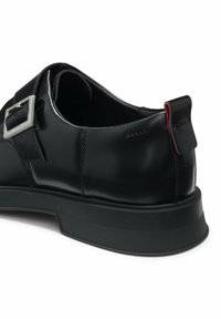 Scarpe nere in pelle con una finitura lucida, caratterizzate da una fibbia rettangolare argentata, forma arrotondata e suola in gomma testurizzata.