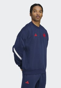 Marineblauwe sweatshirt met rode accenten, voorzien van het Adidas-logo, geribbelde ronde halslijn en witte strepen op de mouwen. Zacht, textuurstof.