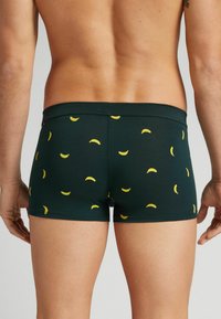 Boxer shorts de color verde oscuro con un estampado repetido de plátanos en amarillo. Tienen una cinturilla suave y elástica, y un diseño ajustado adecuado para la comodidad.