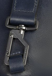 Details van een navy lederen tas met een metalen clip, met een gestructureerd oppervlak, zichtbare stiksels en een accent van een merkriem.