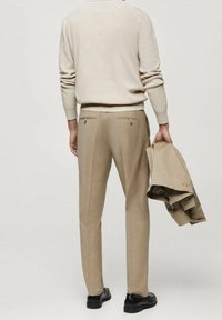Helles beiges Sweatshirt, getragen mit beigen Hosen. Die Hose hat zwei Gesäßtaschen, ist tailliert und wird mit einer passenden Jacke in der Hand kombiniert.