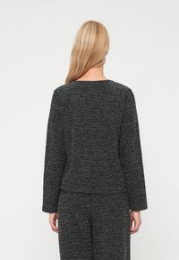 Μαύρο πλεκτό τοπ με υφή, μακριά μανίκια, στρογγυλή λαιμόκοψη και άνετη εφαρμογή, συνδυασμένο με μαύρο παντελόνι.