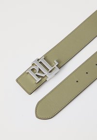 Olive krāsas ādas josta ar sudraba "RL" logotipa sprādzi. Iezīmēta ar redzamām šuvēm, vairākām caurumiem regulēšanai un sašaurinātiem galiem.