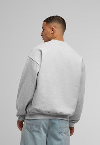 Grå bomulds sweatshirt med drop-skulder og ribbede manchetter, der har en rund hals og en afslappet pasform. Båret med lyseblå jeans.