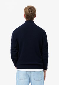 Navy blue knit sweater with a high collar and ribbed cuffs, featuring a fitted design. Pairing with light blue jeans is visible.