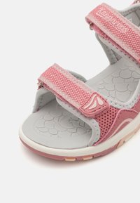 Pink synthetic sports sandal with grey mesh straps, adjustable velcro closures, and textured sole featuring a scale pattern.