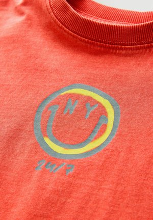 T-shirt rossa in cotone con una grafica rotonda che presenta "NY" in grigio e un contorno giallo, con "24/7" stampato sotto in grigio coordinato.
