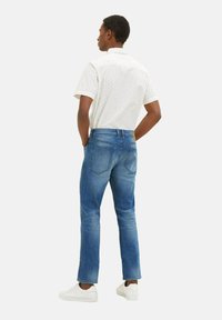 Cămașă cu mânecă scurtă pentru bărbați, albă, cu model mic albastru, asortată cu blugi din denim bleumarin și adidași albi, văzută din spate.