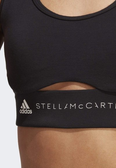 Black sports bra with a rounded neckline, featuring a cut-out detail and elastic band displaying "ADIDAS" and "STELLANMCARTNEY" in white lettering.