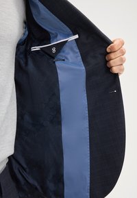 Wnętrze marynarki prezentujące dopasowany krój w kolorze granatowym, kontrastową niebieską podszewkę, detale teksturowe oraz metkę slim-fit.
