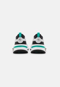 Black and white athletic shoes with turquoise accents, featuring a textured sole and a rear pull tab for easy wear. Distinctive logo on back.