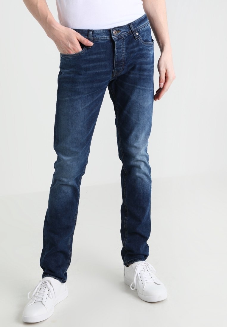 Blå denimjeans med smal passform, femfickorsdesign, urblekta mönster och mässingsdetaljer. Matchas med vita sneakers och en åtsittande vit t-shirt.