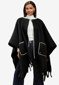 Poncho nero in lana con collo rotondo, bordatura bianca, due tasche frontali e dettagli con frange lungo l'orlo. Design morbido e ampio.