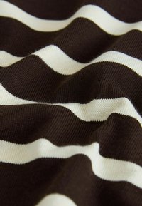 Detailný záber na pokrčenú tkaninu s prestriedavými horizontálnymi čiernymi a bielymi pruhmi pletenými.