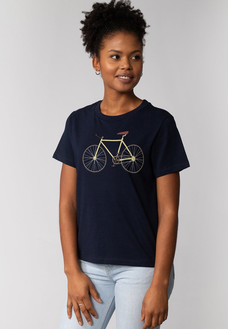Navy katoenen T-shirt met een gele fietsafbeelding. Korte mouwen, ronde hals en een relaxte pasvorm. Model draagt een lichtblauwe spijkerbroek.