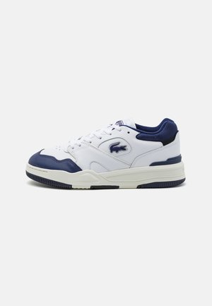 White sneakers with dark blue accents; made of leather and mesh; features a round toe, lace-up design, and textured rubber sole.