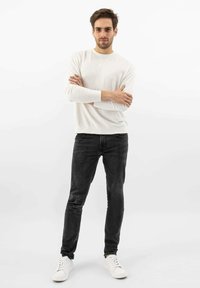 Weißes langärmliges Hemd, kombiniert mit schwarzen Slim-Fit-Jeans und weißen Sneakern. Das Outfit zeichnet sich durch eine glatte Textur und ein lässiges Design aus.