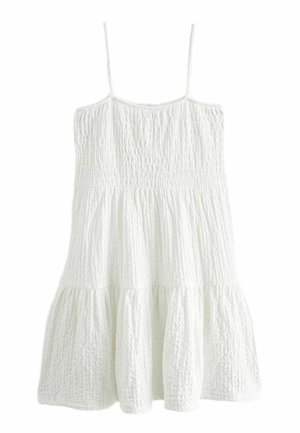 Robe blanche sans manches avec fines bretelles, tissu texturé, corsage smocké ajusté et jupe évasée à étages.