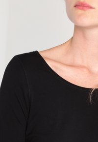 Schwarzes Langarmoberteil mit weicher Textur und einem breiten, abgerundeten Halsausschnitt. Verfügt über dezente Nahtdetails entlang der Kanten.