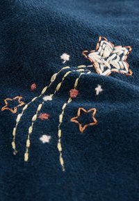 Donkerblauwe stof met een textuur en een kleurrijk borduurontwerp, waaronder een ster en vloeiende lijnen in geel, oranje, roze en wit.