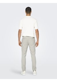 Camisa blanca de manga corta combinada con pantalones claros de tablas grises, con corte recto y dos bolsillos traseros. Zapatillas blancas completan el look.