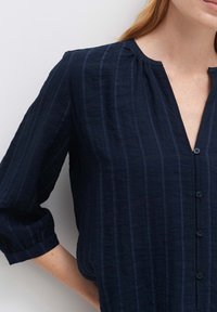 Camicia button-up blu navy con righe verticali, realizzata in tessuto leggero. Presenta un colletto a V e maniche a tre quarti.
