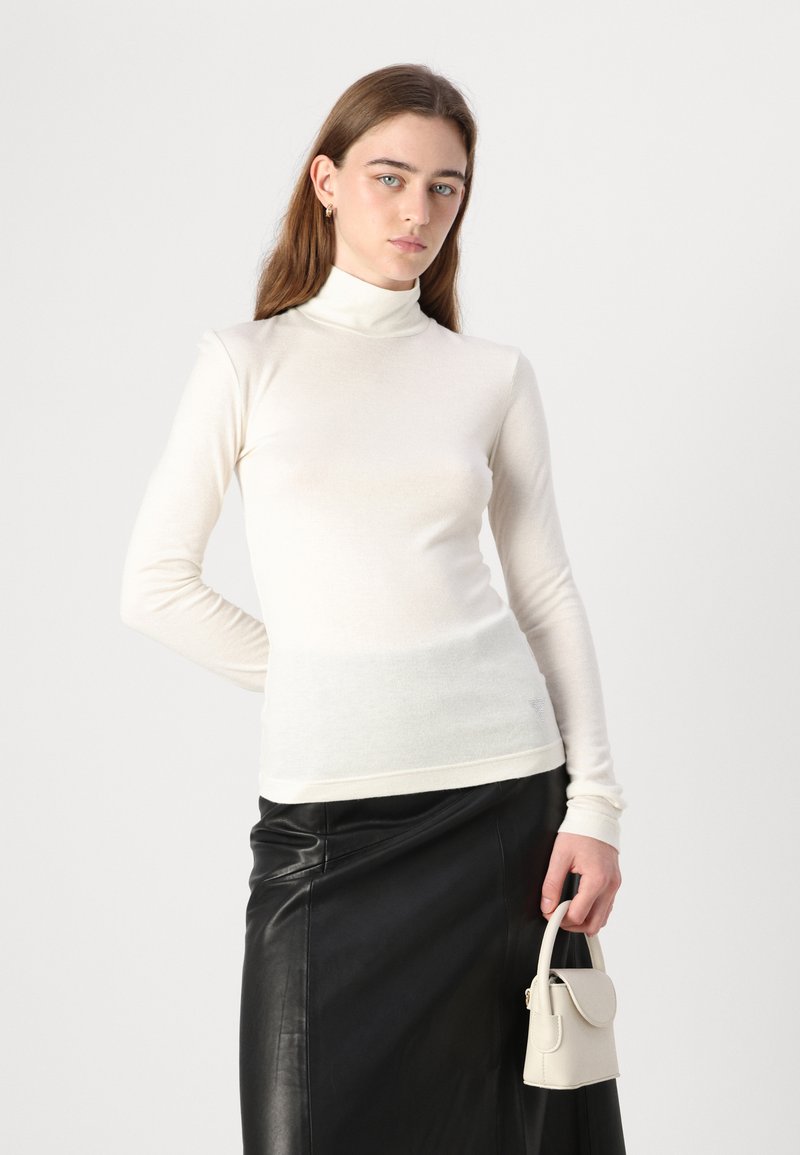 Witte lange mouwen turtleneck top in een zachte, gladde stof, gecombineerd met een zwarte leren rok en een kleine lichtgekleurde handtas.