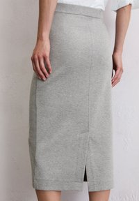 Šedá tužková sukně vyrobená z měkké látky, s rozparkem na zadní straně a hladkým pasem. Design je přiléhavý s minimálními švy.